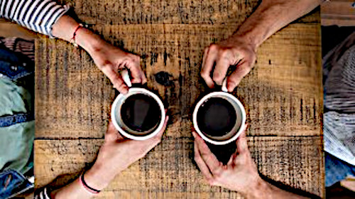 two people sit at a wooden table, each holding a cup of coffee